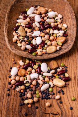 in the foreground, varieties of dried legumes mixed in a large spoon and on a rustic wooden background clipart