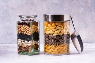 Gri dokulu arka planda İtalyan makarnası çeşitleri ve cam kavanozlarda kurutulmuş baklagiller var. Akdeniz diyeti