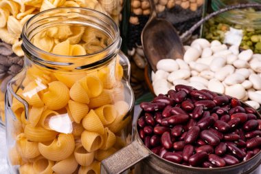 çeşitli kurutulmuş baklagiller ve ön planda cam kavanozlarda İtalyan makarnası.