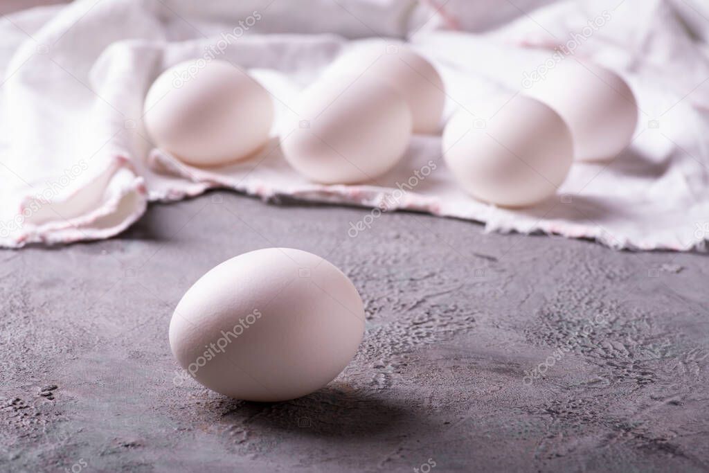 in the kitchen on the gray textured background, in the foreground, fresh white eggs ready for the preparation of homemade culinary recipes