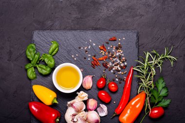 Siyah bir taş, sarımsak, zeytinyağı ve baharat ve bitkilerle dolu sayısız malzeme. Yukarıdan görüntüle