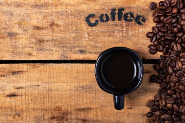 Kaba ahşap bir kutuda, bir fincan sade kahve ve kavrulmuş kahve çekirdeği.