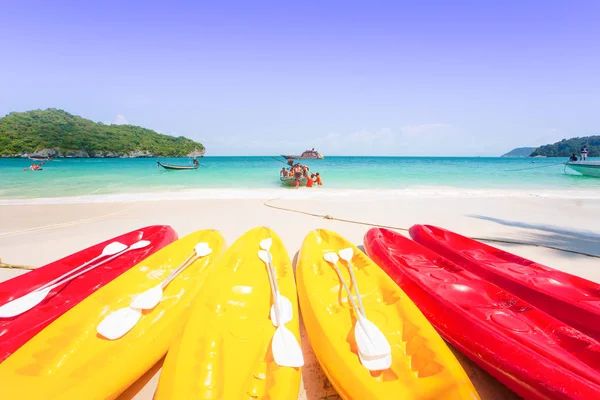 Colorful sea kayak on white sand beach. Tourists, turquoise blue seawater, and light blue sky background.