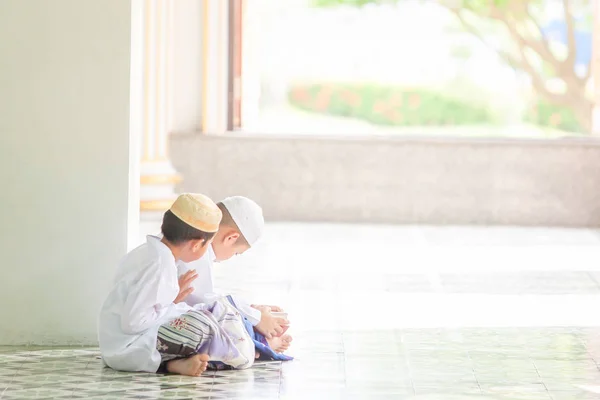 Couple Muslim boy in traditional clothing reading Koran in the m