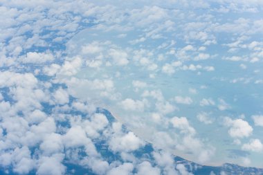 Uçak penceresinden mavi gökyüzünün ve dalga bulutlarının havadan görünümü.