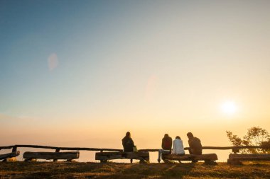 Gün doğumunda bir dağın zirvesinde ki kütüklerde dinlenen bir grup turist. 