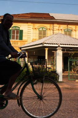 Laos 'lu son sınıf öğrencisi bisikletle eski Fransız Koloni evinin önünden geçiyor..