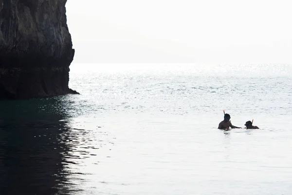 Néhány turista búvárkodik a tengerben az ősi szikla előtt.. — Stock Fotó