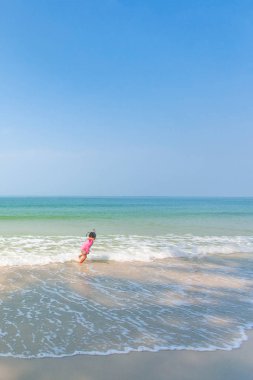 Su 'da tropik plajlarda koşan ve oynayan sevimli küçük bir kız.