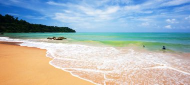 Güneşli bir yaz günü okyanus sörfünde oynayan iki Avrupalı çocuk açık mavi gökyüzünün altında altın kum plajları resmediyor. Khao Lak, Tayland.