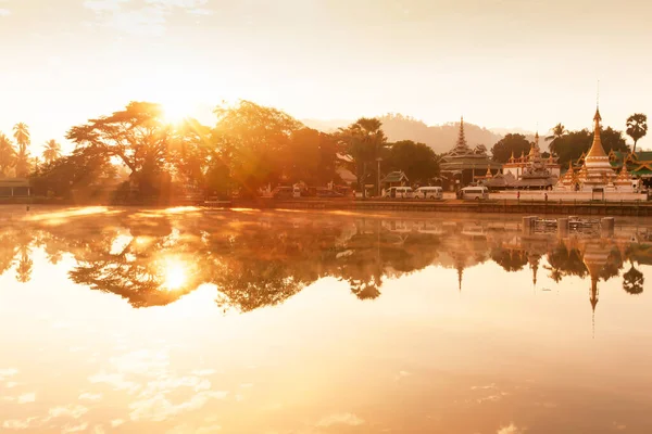 A tranquil landscape of lake and ancient buddhist temple at sunrise, glowing golden sun shines on the lake and ancient temple, famous place in Mae Hong Son, North Thailand.