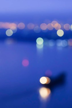 Mavi bir gecede nehir kenarındaki Defocus şehir manzarası, parlak ve renkli bulanık bokeh daireli renkli ışıklar, nehirdeki konteyner gemisi, yaratıcı arkaplan için soyut Bokeh. Boşluğu kopyala.