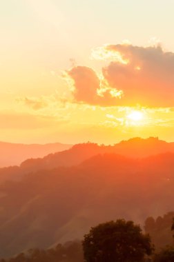 Gün batımında muhteşem dağ manzarası, bulutların ve sıradağların ardında parlayan güneş. Pozitif duygu kavramı. Yumuşak odak.