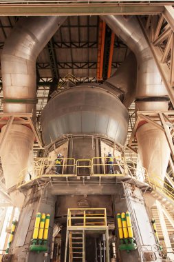 İki erkek mühendis koruyucu ekipman giyip bir fabrikada büyük makineleri tamir ediyor..