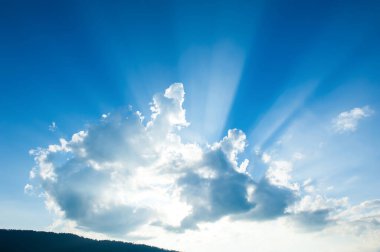 Güneş ışınları bulutların arasından bir dağ sırasının üzerinde parlıyor. Arka planda mavi gökyüzüne karşı çarpıcı ışık huzmeleri. İlham konsepti.