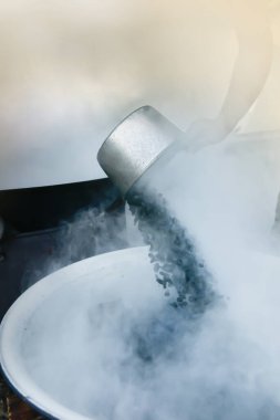 Geleneksel bir şekilde kahve çekirdeklerini kavuran Asyalı bir kadın. Gümüş kepçeye odaklan.