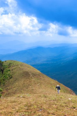 Dağların zirvesinde yürüyüş yapan yaşlı bir adam. Arka planda sihirli mavi bulutlar ve dağ sıraları..
