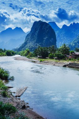 Nam Song Nehri manzarası ve nehir kıyısındaki eski bir köy, muhteşem kireçtaşı sıradağları ve arka planda mavi bulutlar, Kuzey Laos kırsal kesiminde.