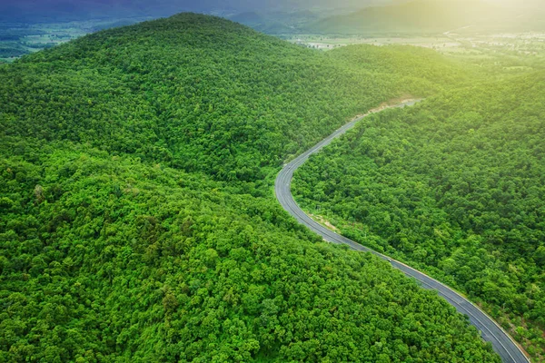 Gün doğumunda dağ yolunun havadan görünüşü, dağ sıralarında asfalt yol ve yeşil orman..