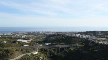Otobanda deniz ve sahil binaları olan bir köprüden geçen arabalar.