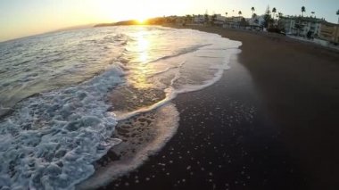 Gün batımında dalgalar sahile ulaşırken sahilde yürümek.