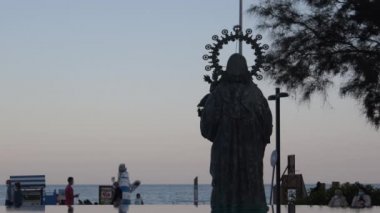Gün batımında yürüyen insanlarla birlikte gezinen bakire heykel silueti.