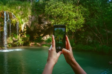 Bir kız ile bir telefon onun elinde bir şelale bir fotoğraf çeker