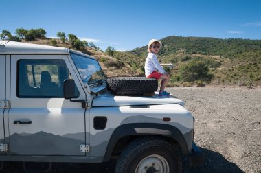 Kırsal Andalucia. İspanya. 06/10/2016. Küçük kız 4 x 4 arazi aracı kaporta mahallede üzerinde açık yedek lastik üzerinde otururken manzaranın.