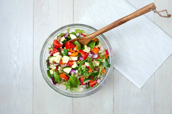 Salata için taze ve sağlıklı sebzeler beyaz ahşap bir yüzeye yerleştirilmiş cam bir kasede..