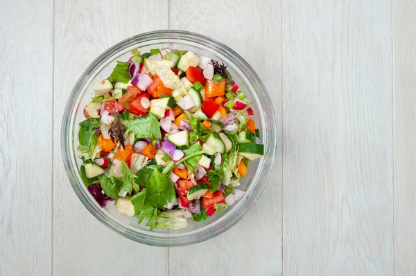 Salata için taze ve sağlıklı sebzeler beyaz ahşap bir yüzeye yerleştirilmiş cam bir kasede..