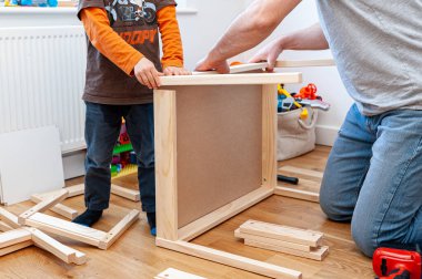 Oğlu olan bir erkek ebeveyn, çocuğun odası için düz paket mobilya montajı yapıyor. Küçük masalı iki küçük sandalye..