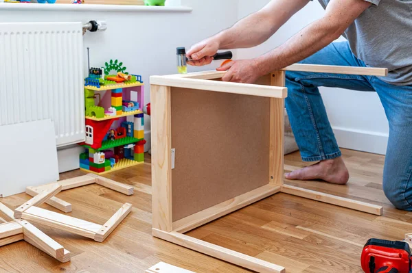 Yetişkin bir erkek çocuk odasında masası olan iki küçük sandalyeyi bir araya topluyor..