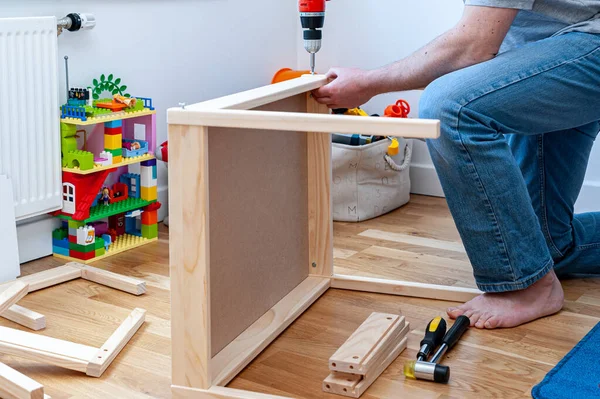 Yetişkin bir erkek çocuk odasında masası olan iki küçük sandalyeyi bir araya topluyor..