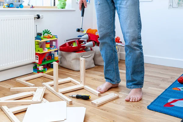 Yetişkin bir erkek çocuk odasında masası olan iki küçük sandalyeyi bir araya topluyor..