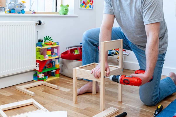 Yetişkin bir erkek çocuk odasında masası olan iki küçük sandalyeyi bir araya topluyor..