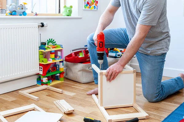 Yetişkin bir erkek çocuk odasında masası olan iki küçük sandalyeyi bir araya topluyor..