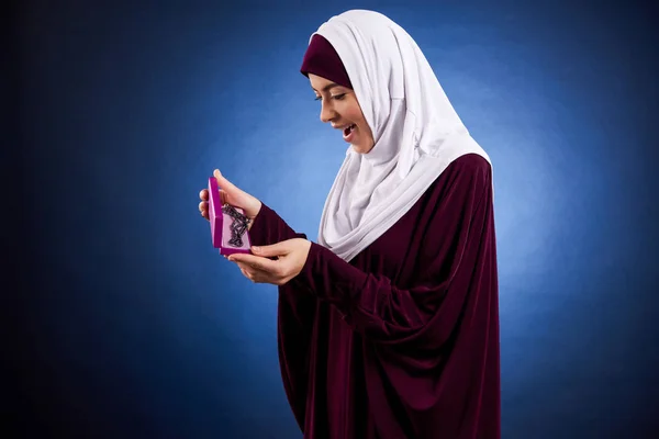 Arab woman in hijab admires necklace in box.