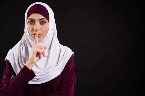 Arab woman in hijab shows gesture quietly.