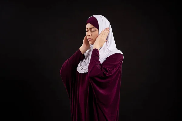 Arab woman in hijab covers ears with hands.