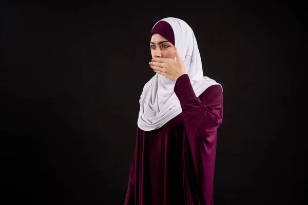 Arab woman in hijab covers mouth with hands.