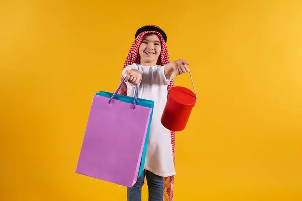 Niño árabe en keffiyeh sostiene bolsas de papel y cajas . — Foto de Stock