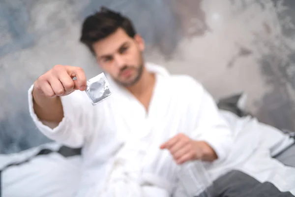 Close up homem segurando preservativo no quarto foco macio — Fotografia de Stock