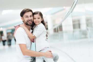Kızı Baba'nın kucağına alışveriş merkezi içinde oturuyor. Baba ve kız gülümseyerek.
