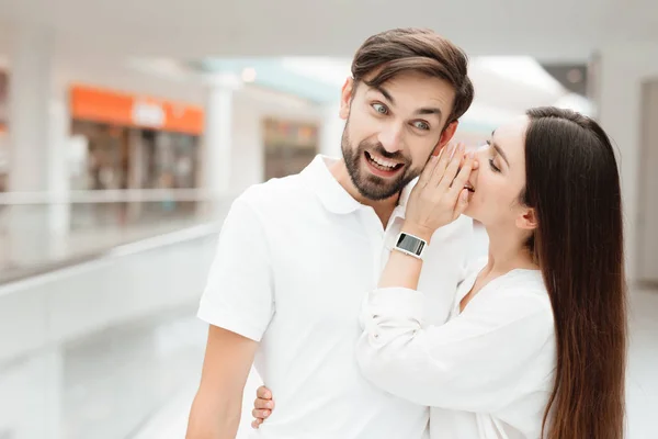 Man and woman in shopping mall. Girl is whispering in man's ear. — Stock Photo, Image