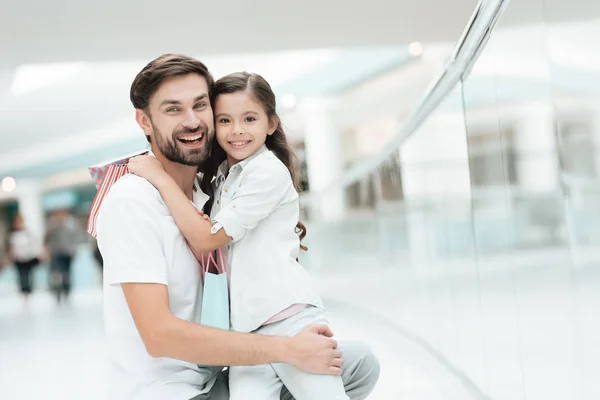 Daughter is sitting on father's lap in shopping mall. Dad and girl are smiling. — Stock Photo, Image