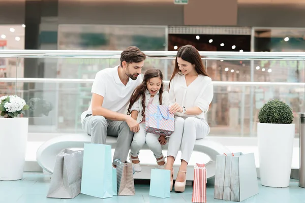 Familie, Vater, Mutter und Tochter sitzen auf Bank in Einkaufszentrum. Mädchen blickt in eine Tasche. — Stockfoto