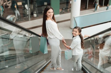 Anne ve kızı alışveriş alışveriş merkezinde yürüyen merdiven üzerinde gidiyorlar.