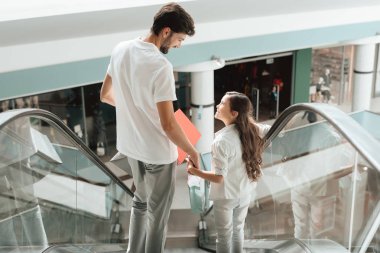 Father and daughter are going down on escalator in shopping mall.