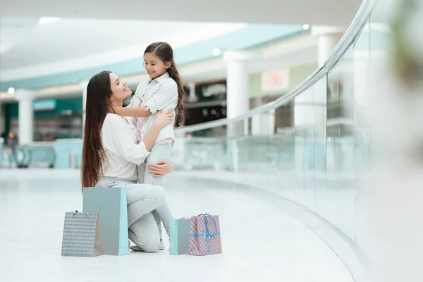 A filha está sentada no colo da mãe no centro comercial. Mãe e menina estão sorrindo . — Fotografia de Stock