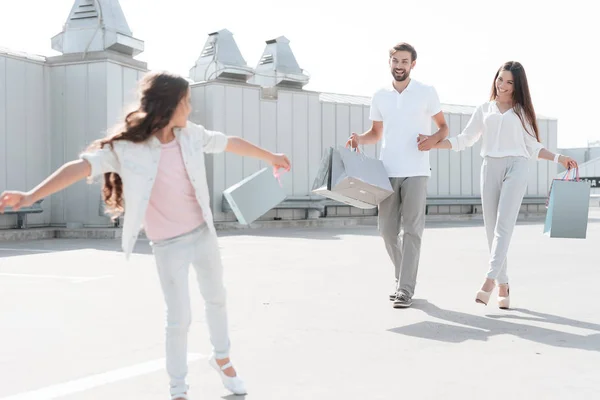 Familia, padre, madre e hija están caminando por la carretera cerca del aparcamiento después de ir de compras en el centro comercial . — Foto de Stock